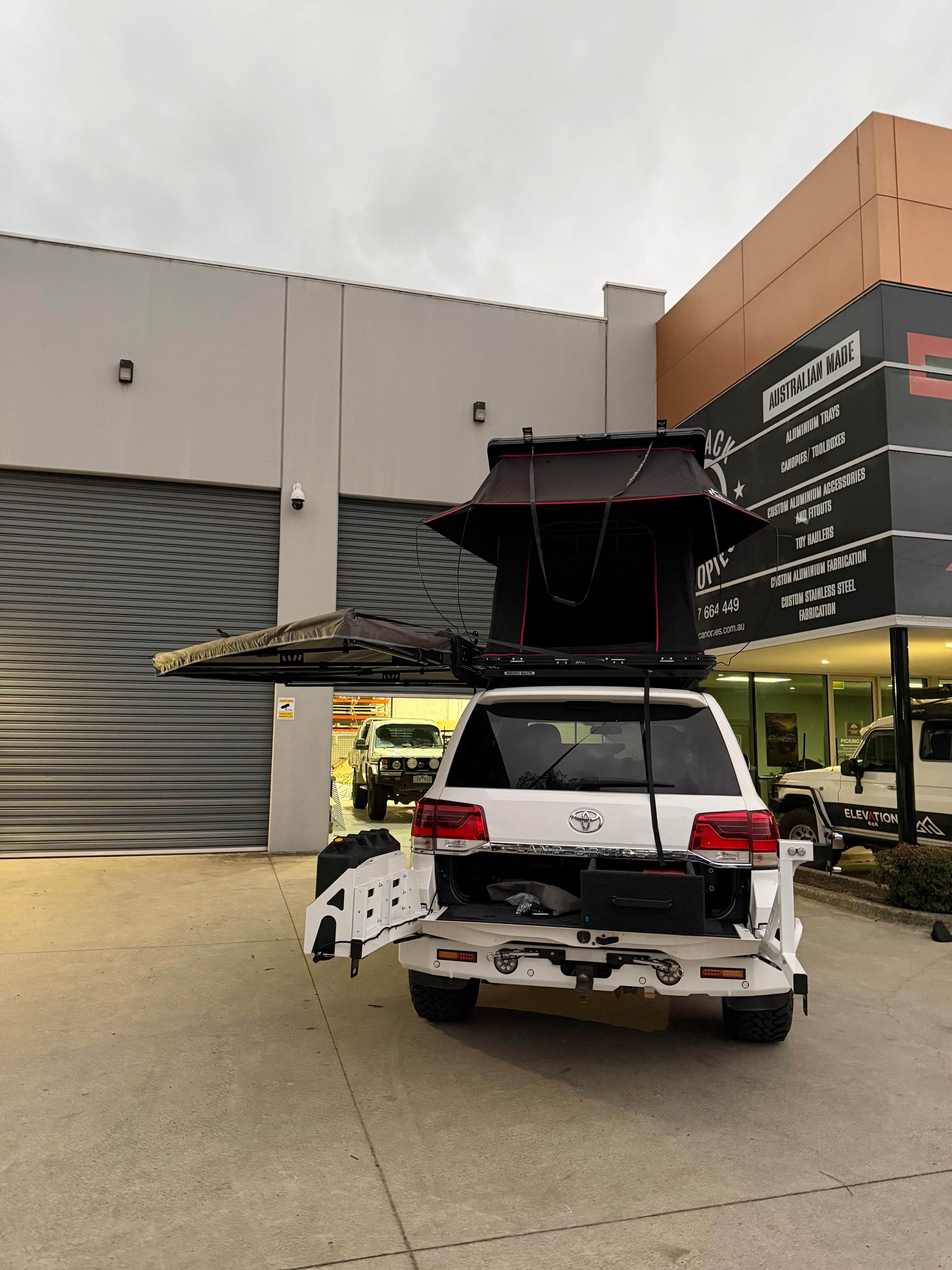White SUV with a roof top tent and awning open in front of a building.