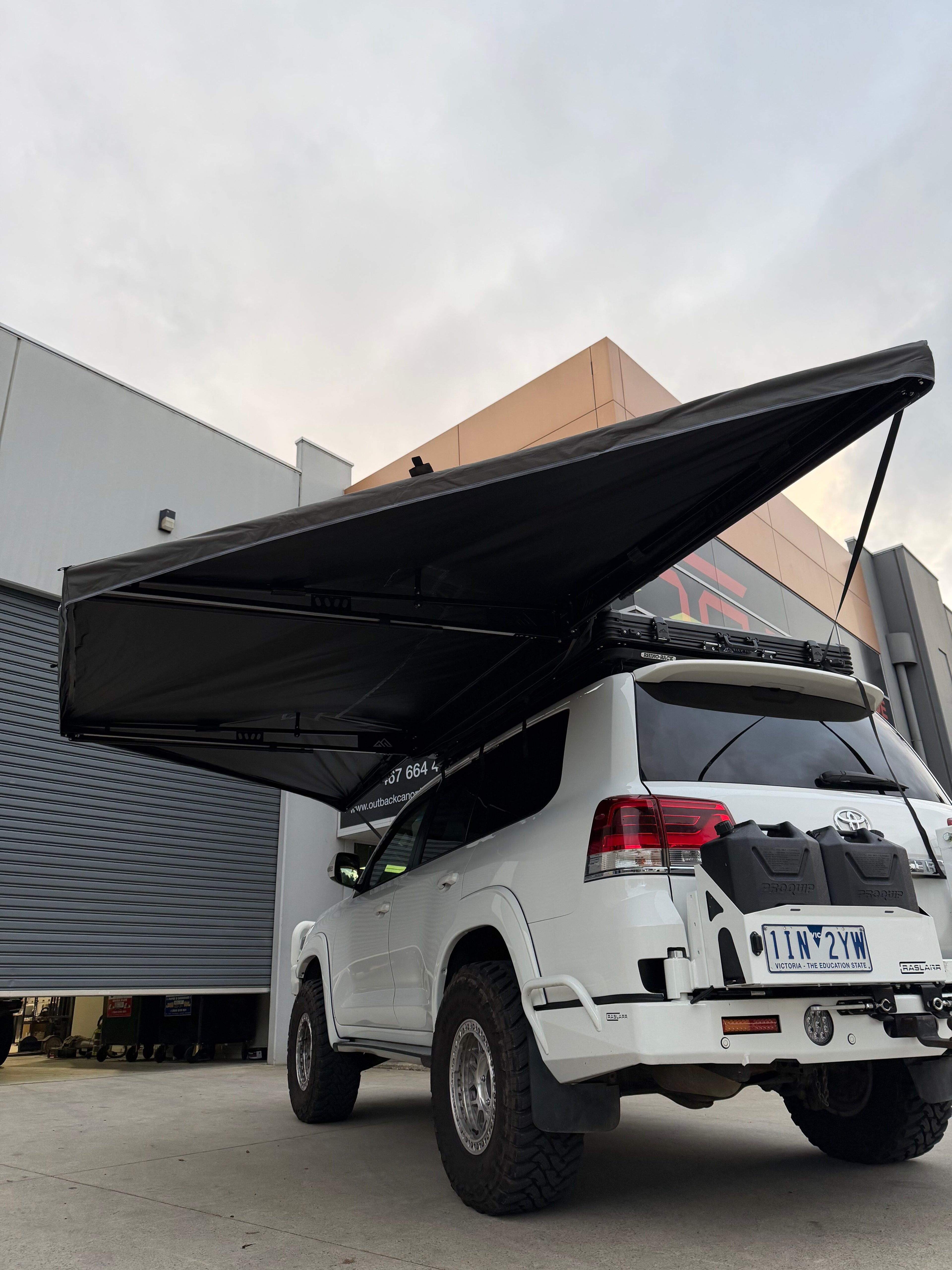 White 200 Series Landcruiser with an extended black awning in front of a building